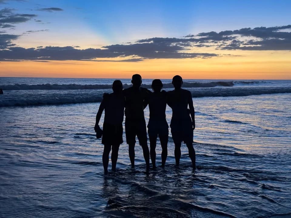 Four friends standing at the shoreline after sunset